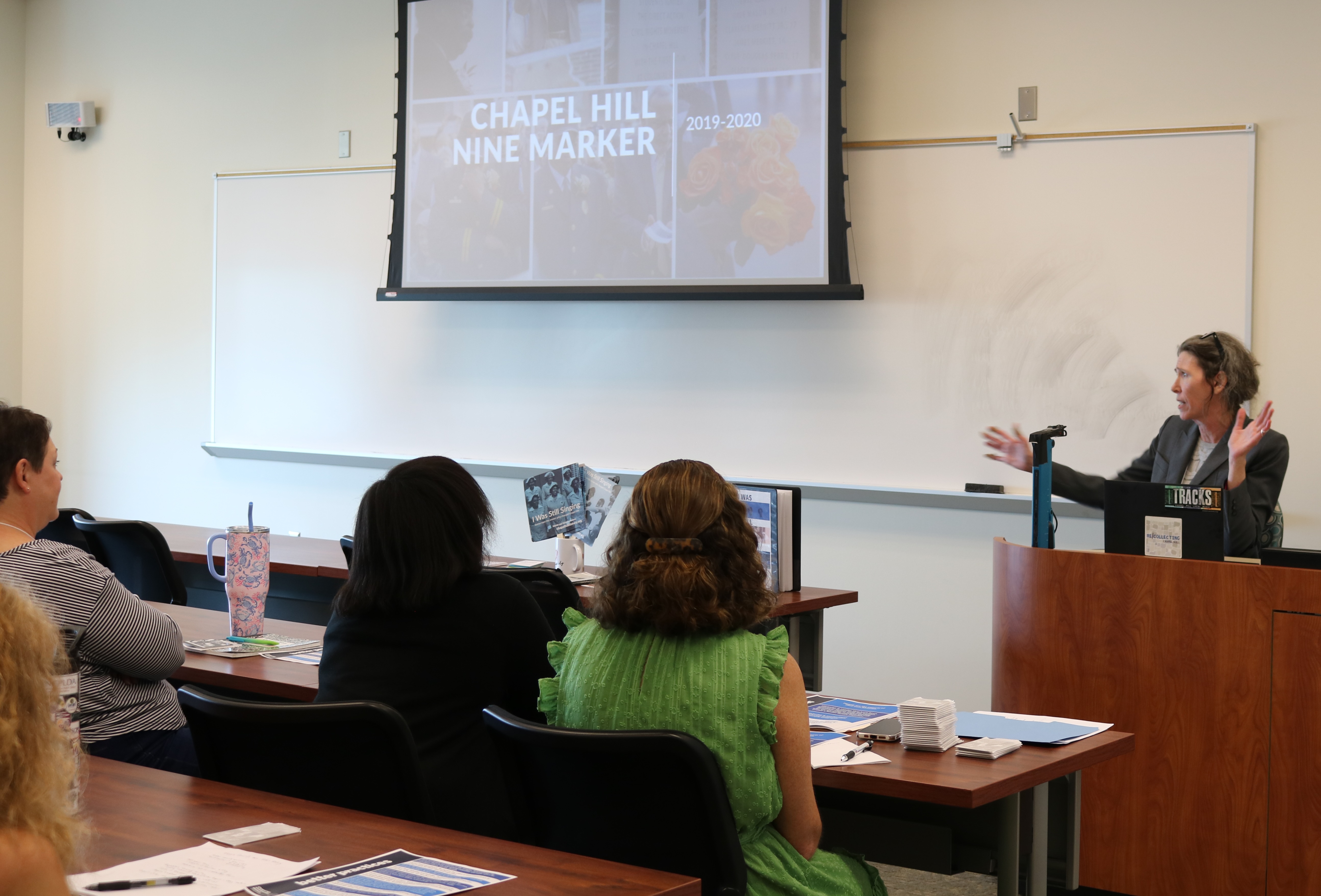 Molly Luby presenting a slide on a projector screen in front of librarians seated at desks.