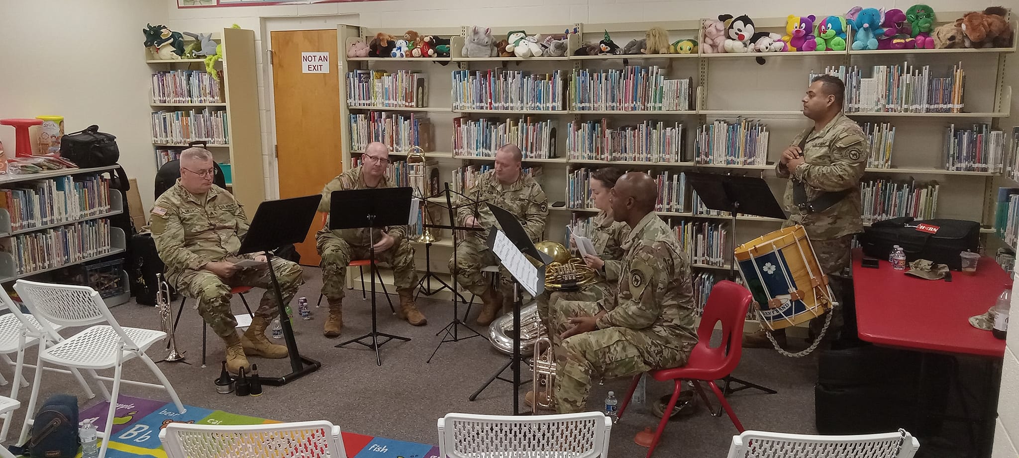 The 208th Army Band jazz quintet seated and playing their instruments in front of library shelves.