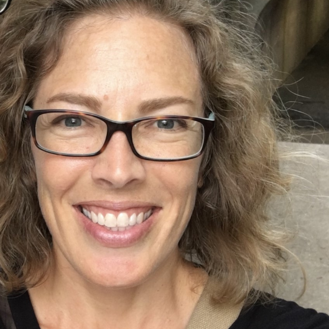 A white woman with curly hair and black glasses.