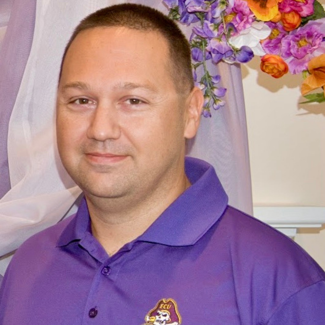 A white man with short, brown hair wearing a purple ECU polo.