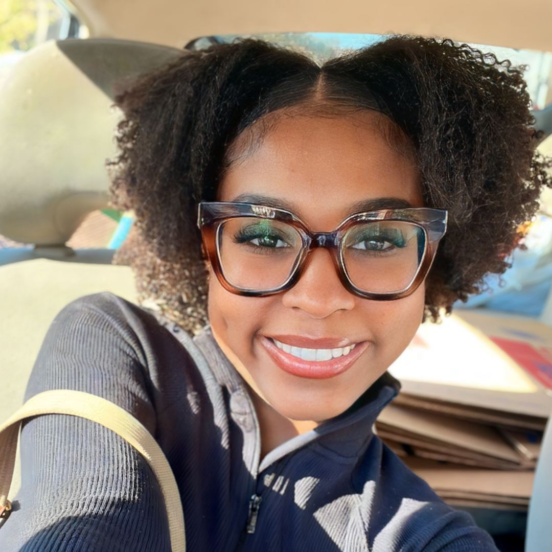 A black woman with curly hair and brown glasses.