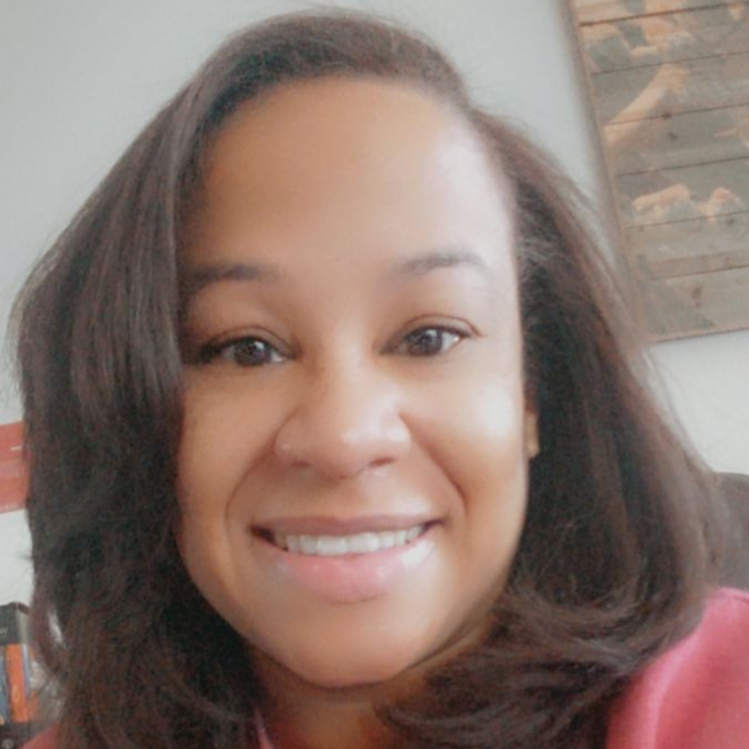 A black woman with shoulder-length brown hair wearing a pink sweatshirt.